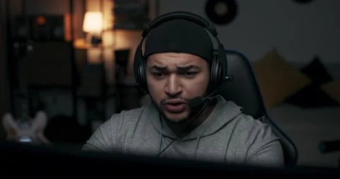 Close-up of guy in black cap playing online game. Man has headphones on head and Stock Footage 214204856