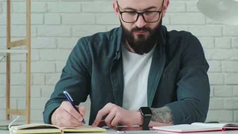 Close up of guy that learn online courses using a tablet and write notice in his Stock Footage 169400049