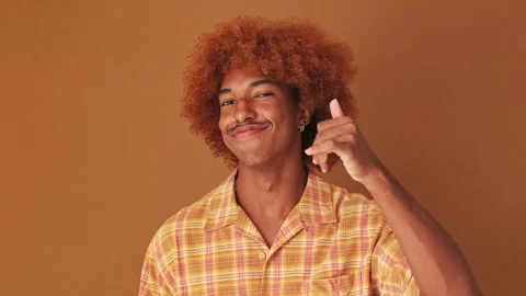 Close up, guy shows call me phone hand sign gesture, isolated on brown Stock Footage 254914124