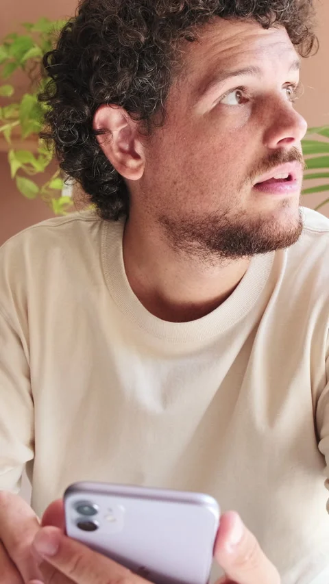 Close up, guy sits on the sofa in cozy living room, holding the phone in his Stock Footage 252030893
