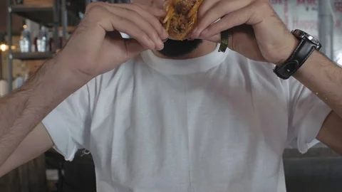 Close-up of a guy in a white t-shirt bites a juicy burger. man eats a hamburger Stock Footage 115634271