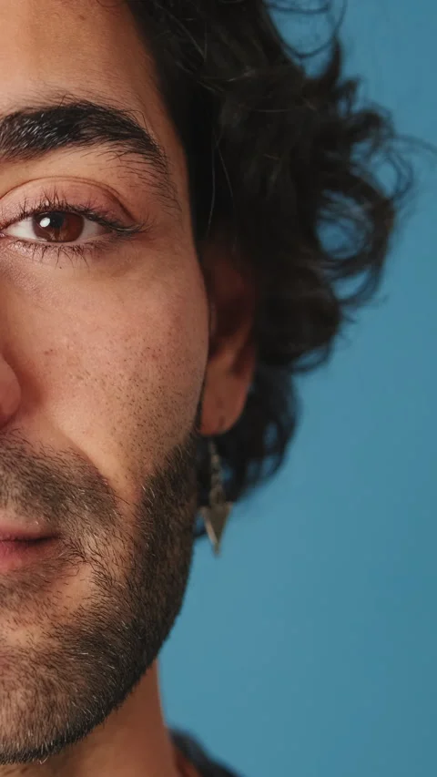 Close-up, of half-face man opens his eyes and looks at camera isolated on blue Stock Footage 254913106