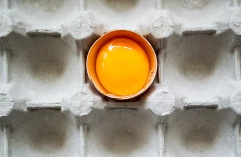 CLose-up half of fresh egg with bright yolk in paper tray for eggs . Top view Stockfoto's