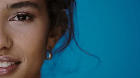 Close-up of half mulatto face looking to camera and blinking with smile on blue Stock Footage 124919354