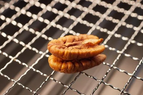 Close-up of a half pecan kernel on a metal grill mesh, natural texture and li Stock Photos