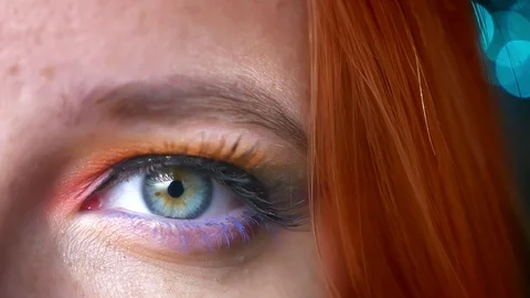 Close-up half-portrait of ginger female colourful eye make-up on blurred blue Stock Footage