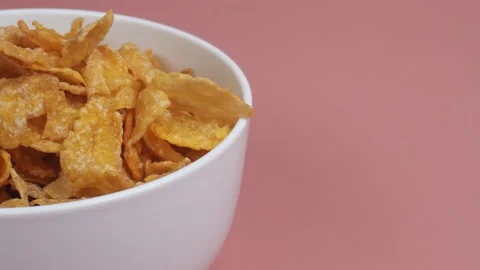 Close up half shot of pouring corn flakes into white bowl on pink background Stock Footage 280023984