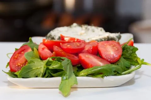 Close up of halved cherry tomatoes with rocket leaves served on white plate Stock Photos