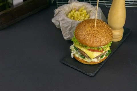 Close-up hamburger on a graphite stand, next to it are fries, tomatoes and pe Stock Photos