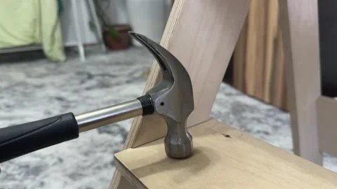 Close-up of a hammer gently tapping on a light wooden surface. Calm DIY gesture Stock Footage 336524202