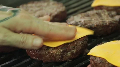Close up of hand adding cheese on top of hamburger patties sitting on a hot g Stock Footage 127716017