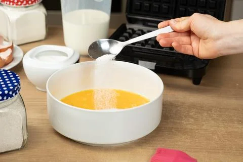 Close-up of a Hand Adding Sugar with a Spoon into a Bowl of Whisked Eggs for Stock Photos