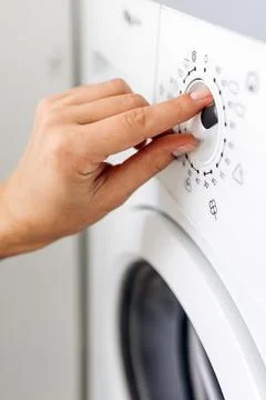 Close-up of a hand adjusting the control dial on a modern washing machine, .. Stock Photos