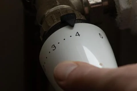 Close up hand adjusting heating temperature. Reducing heating cost in crisi.. Stock Photos