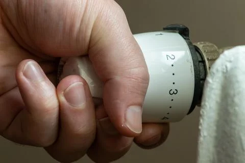 Close up hand adjusting heating temperature. Reducing heating cost in crisi.. Stock Photos