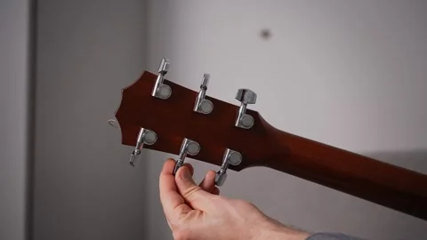 Close-up of a hand adjusting the tuning peg on an acoustic guitar headstock. The Stock Footage 295339629