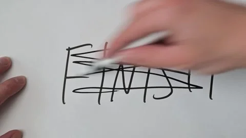 A close-up of a hand aggressively crossing out the word "Finish" with a black 库存影片 337550811