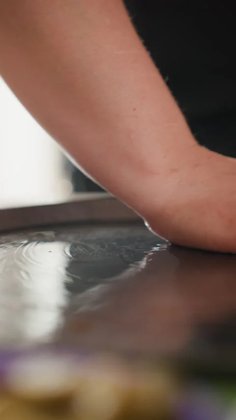 Close-up hand and forearm smoothing dough across glossy dark countertop with Stock Footage 343680314