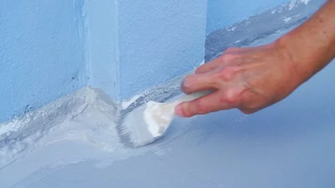 Close up of a hand applying grey waterproofing coating to a blue wall corne.. 動画素材 331629149