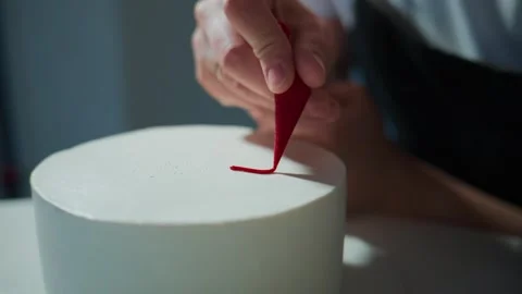 Close-up of hand applying red icing to a pristine white cake surface Stock Footage 336090365