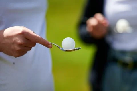 Close up of a hand balancing a white table tennis ball on a metal spoon durin Foto stock
