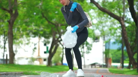 Close-up hand in a blue glove picking up a plastic bottle from a park path. 스톡 동영상 346584409