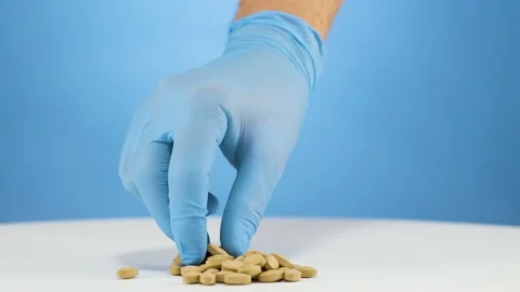 Close-up hand blue gloves picking up a brown zinc supplement tablet, Video stock 238795756