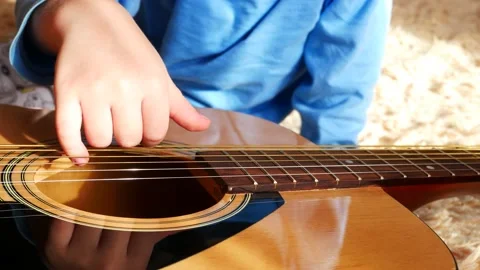 Close-up of the hand of a boy trying to play a guitar pulling the strings Video stock 149599024