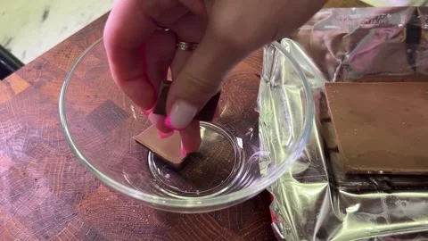Close-up of a hand breaking milk chocolate pieces into a glass bowl, prepar.. Stock Footage 317945498