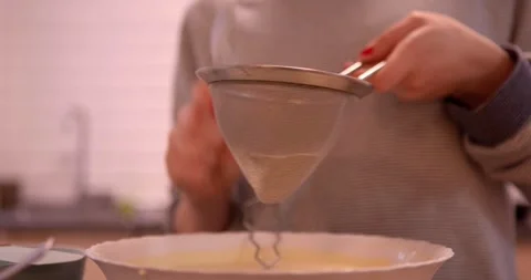 A close-up of a hand carefully sifting fine powder into a bowl Stock Footage 331399707