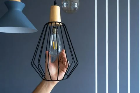 Close-up. A hand changes a light bulb in a stylish loft lamp. Spiral filament Stock Photos