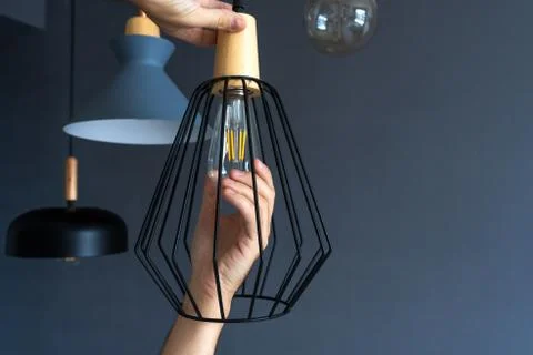 Close-up. A hand changes a light bulb in a stylish loft lamp. Spiral filament Stock Photos