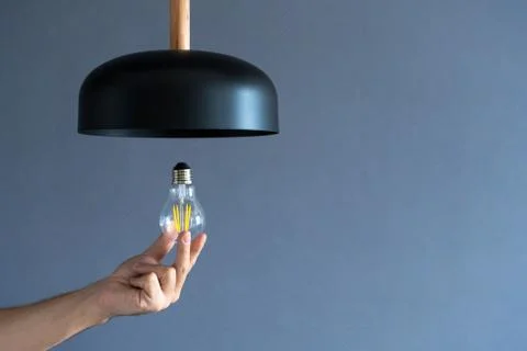 Close-up. A hand changes a light bulb in a stylish loft lamp. Spiral filament Stock Photos