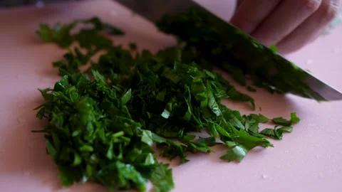Close up of hand chopping fresh green parsley with knife on pink cutting boar 库存影片 340036089