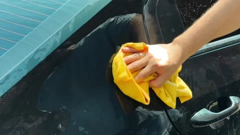 Close-up of hand cleaning black car with yellow cloth in sunlight, 4K car wash 库存影片 340253656