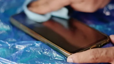 Close-up of a hand cleaning a smartphone screen with a microfiber cloth for.. 動画素材 338225397