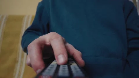 Close up of a hand clicking buttons on a TV remote control to change channels.	 Stock Footage 330361353