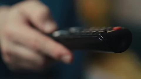 Close up of a hand clicking buttons on a TV remote control to change channels.	 Video stock 330361433