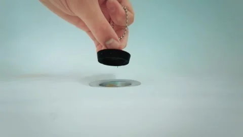 Close up hand closing bathtub drain with black rubber stopper on metal chain Stock Footage 346285331