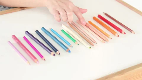 Close-up of a hand counting colored pencils arranged by color gradient on a whit Stock Footage 331514290