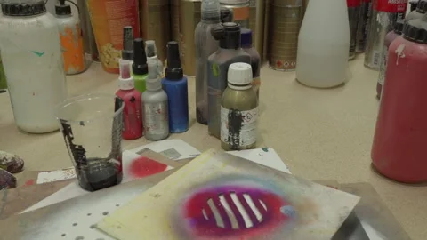 A close-up of a hand-cut stencil and various liquid pigments in a creative Stock Footage 335964754