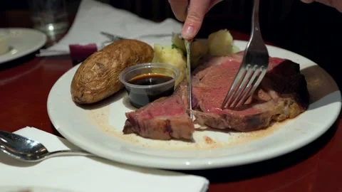 Close up hand cuts into prime rib meal at restaurant Stock Footage 133466617