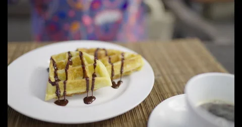 Close up of a hand cutting and eating golden waffles topped with chocolate sauce Видео 340310122