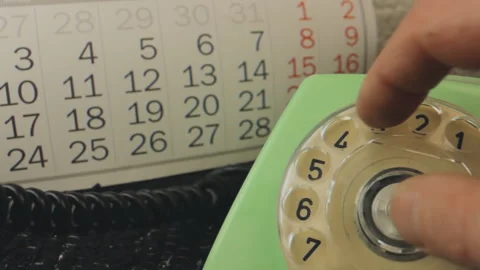 Close-up hand dialing a vintage green rotary telephone with a wall calendar Stock Footage 337737788