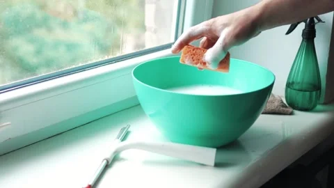 Close up of a hand dipping an orange sponge into a basin with soapy foam on.. Видео 340159525