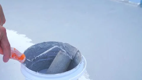 A close-up of a hand dipping a paint roller into a bucket of grey waterproo.. 스톡 동영상 331629147