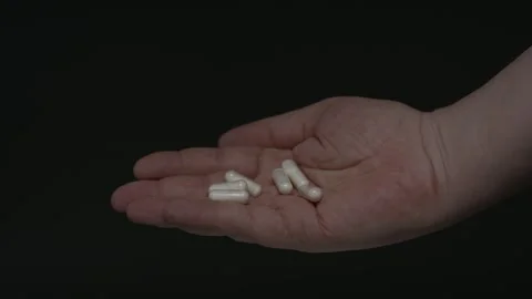 Close-up of a hand displaying multiple capsules in the palm against a black Stock Footage 338443445