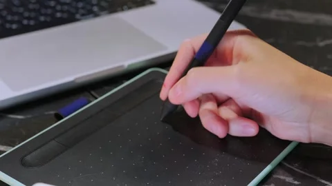 Close-up of a hand drawing on a graphic tablet using a stylus pen, creating 库存影片 333581281