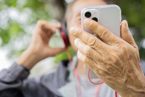 Close-up hand of elder man holding phones and listening to music outdoor in.. Stock Photos