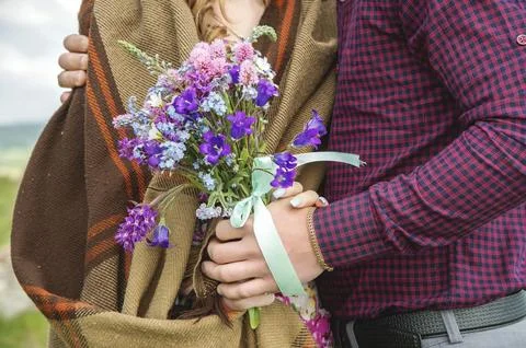 Close-up of a hand embracing a pair of guy and his girlfriend with bouquet. Stock Photos